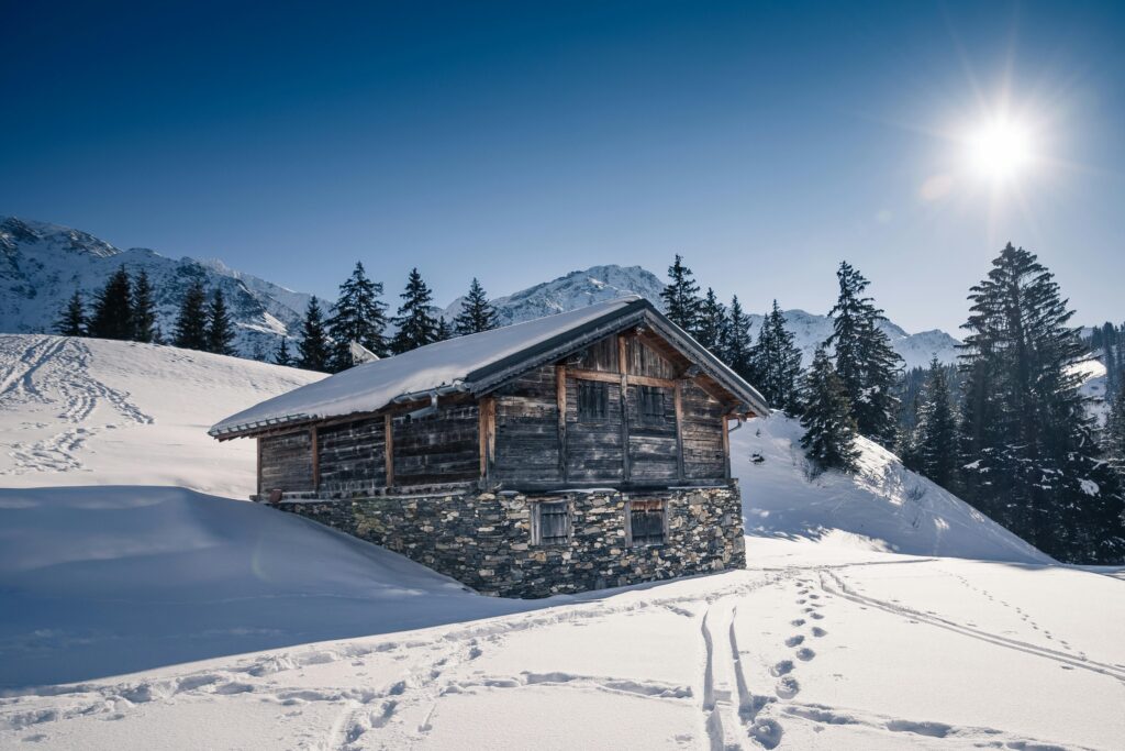 Charming rustic chalet in snowy French Alps with bright sun and mountain backdrop.